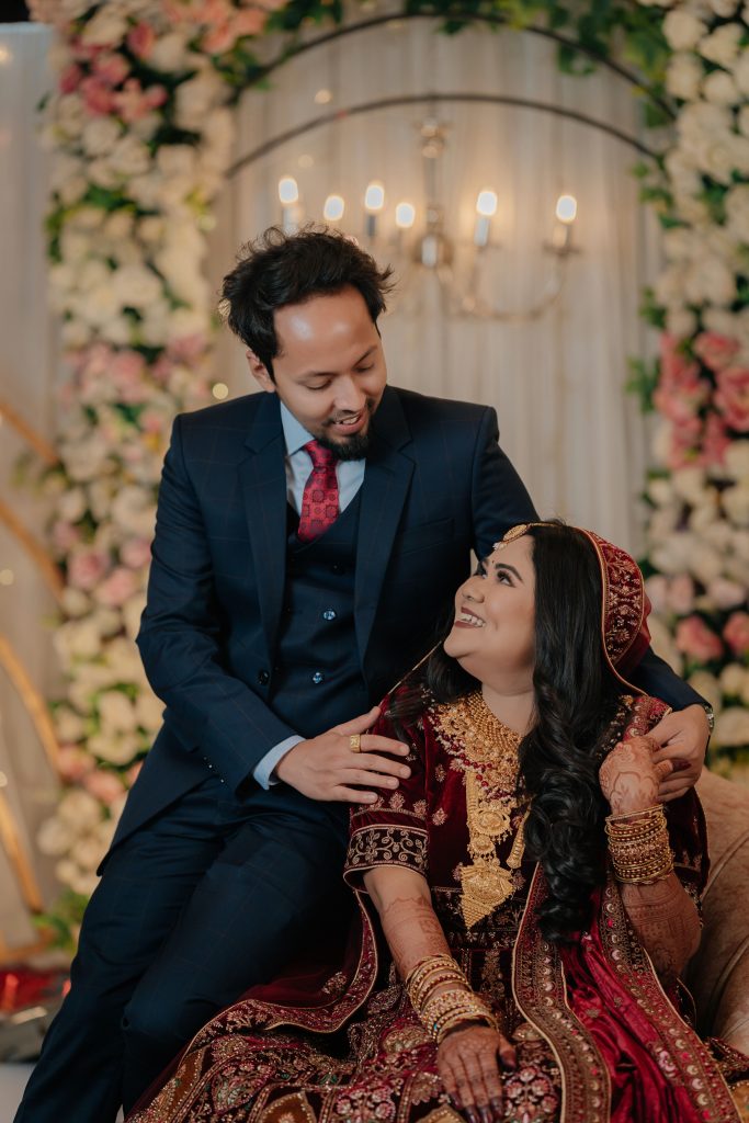Joyful South Asian couple dressed in traditional attire, celebrating their wedding indoors.